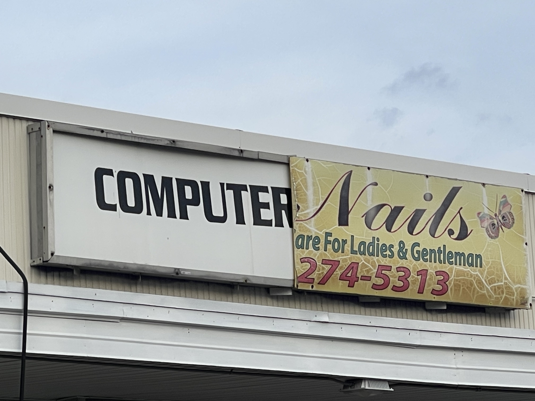 Sign with half fallen off and old part showing. Left reads “computer” and right “nails”.