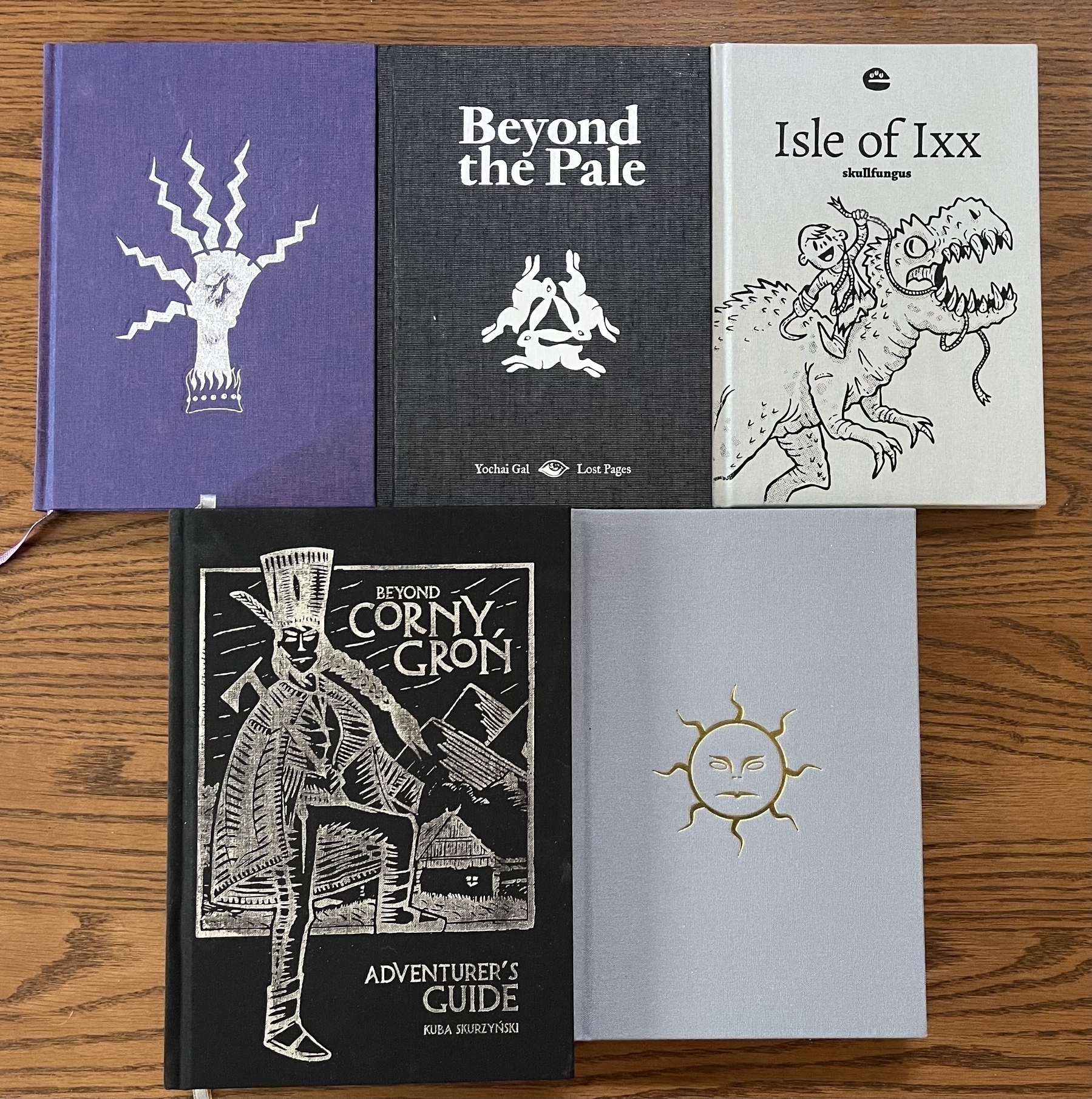 Five illustrated book covers are laid out on a wooden surface, each featuring unique artwork and titles.