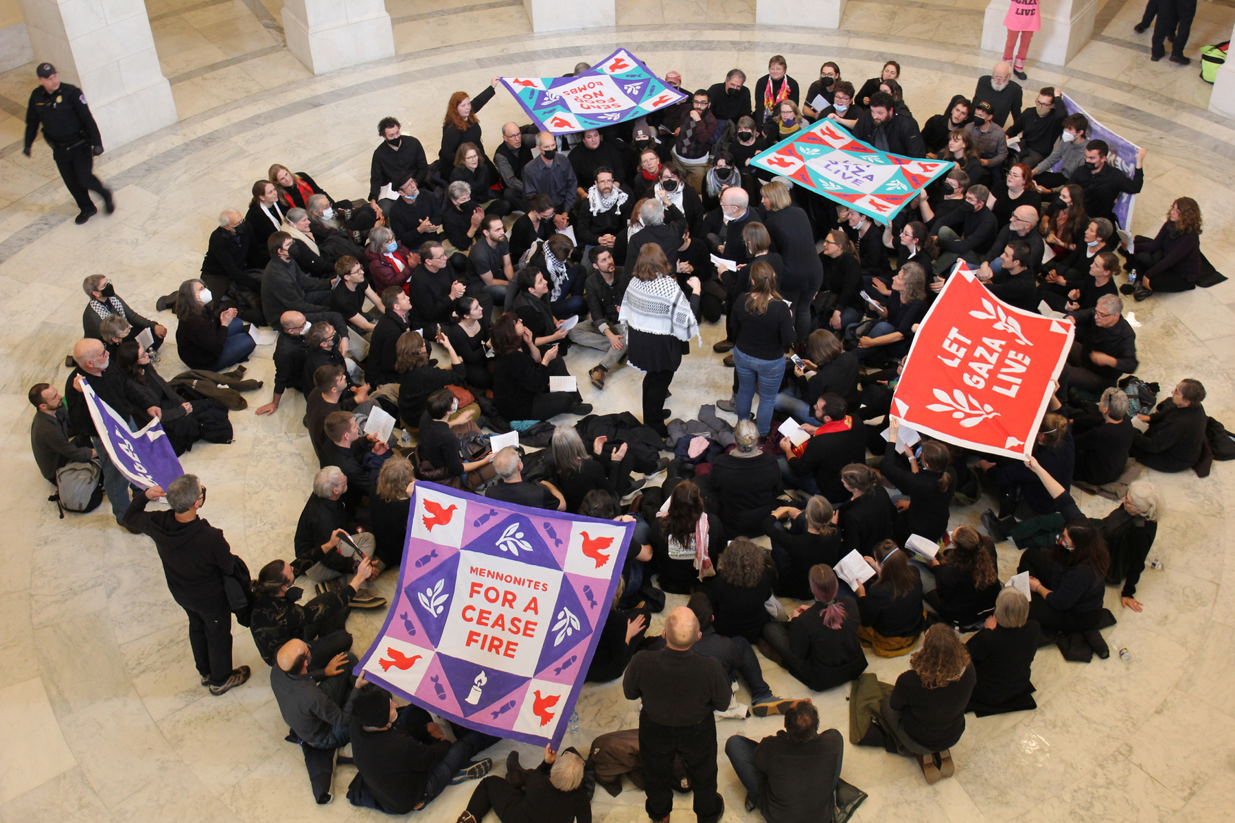 overhead shot of Mennonites sitting and singing, with their quilted banners