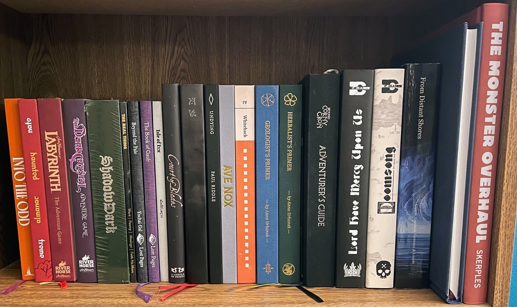 A collection of role-playing game books and sourcebooks is neatly arranged on a wooden shelf. 